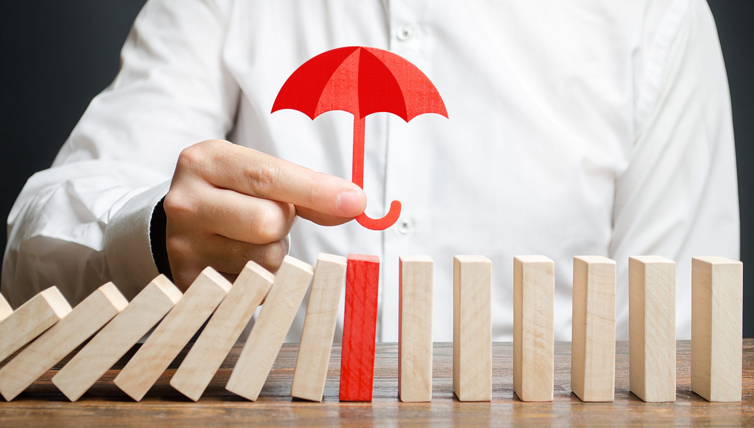 A businessman insures red dominoes and stops the collapse of the whole system. Insurance and risk management. Accurate forecasts and miscalculations. Financial support, subsidies and exemptions